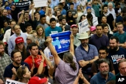 A woman holds up a sign for Democratic presidential candidate Hillary Clinton as she is escorted out during a rally for Republican presidential candidate Donald Trump, in San Jose, Calif., June 2, 2016.