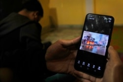 Myanmar refugees who have fled violence in Chin state, northwestern Myanmar, watch photos and videos of burning structures back home, at an unspecified location in India, Dec. 13, 2021.
