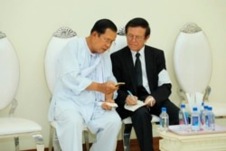 FILE - Cambodian Prime Minister Hun Sen, left, talks with dissolved main opposition Cambodia National Rescue Party leader Kem Sokha at the mourning ceremony of Sen's mother in-law, in Phnom Penh, Cambodia, Tuesday, May 5, 2020. Cambodian Prime Minister Hun Sen met Tuesday with an opposition leader whose political party was dissolved after he was charged with treason. (Pool via AP)