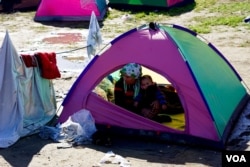 A woman and child huddle in a tent in a makeshift encampment in Idomeni, Greece, waiting for permission to move onto other points in Europe, March 4, 2016. (J. Dettmer for VOA)