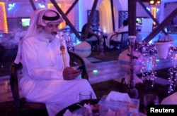 FILE - A Saudi man uses his smartphone as he smokes water pipe at a cafe in Dammam, Saudi Arabia, March 7, 2016.