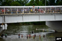 Honduran migrants heading in a caravan to the US, wait to help fellow men get down to the Suchiate River from the Guatemala-Mexico international border bridge, in Ciudad Hidalgo, Chiapas state, Mexico, Oct. 20, 2018.