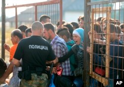 A Macedonian border policeman opens a gate for the refugees and migrants to reach the southern Macedonian town of Gevgelija, Sept. 11, 2015. Hundred of thousands migrants and refugees trying to reach the heart of Europe via Turkey, Greece, the Balkans and