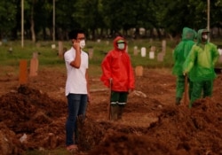 Firos Justin Sumantri, putra Ratih Purwarini, seorang dokter yang meninggal karena COVID-19, berdoa saat petugas kota menunggu, di samping makam ibunya saat pemakaman di Jakarta, 31 Maret 2020. (Foto: REUTERS/Willy Kurniawan )