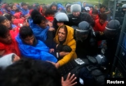 Slovenian policemen keep order as migrants attempt to board the first bus after opening the border with Slovenia in Trnovec, Croatia, Oct. 19, 2015.