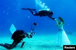 A model opens her mouth to breathe from a scuba tank as Israeli photographer Johannes Felten (L) takes pictures during an underwater photo shoot in the Red Sea in the resort city of Eilat, Oct. 22, 2013.