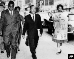 Dr. Martin Luther King Jr. under arrest by Atlanta Police Captain R.E. Little, left rear, passes through a picket line in front of a downtown department store on Oct. 9, 1960.