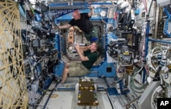 FILE - In this April 9, 2015, file photo made available by NASA, astronauts Terry Virts, bottom, and Scott Kelly perform eye exams in the Destiny Laboratory of the International Space Station as part of ongoing studies on vision health in microgravity.