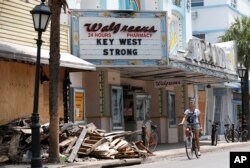 FILE - A cyclist rides past a pile of debris, Sept. 21, 2017, in Key West, Fla.