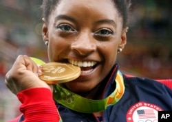 United States' Simone Biles bites her gold medal for the artistic gymnastics women's individual all-around final at the 2016 Summer Olympics in Rio de Janeiro, Brazil, Aug. 11, 2016.