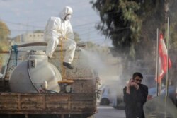 A municipal worker wearing protective gear sprays disinfectant as a precaution against the coronavirus outbreak as a man speaks on his mobile phone, in the suburb of Beir Hassan, Beirut, Lebanon, Monday, March 16, 2020. (AP Photo/Hassan Ammar)