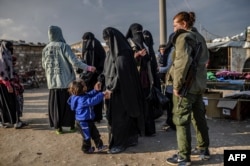 Veiled women, reportedly wives and members of the Islamic State, walk under the supervision of a female fighter from the Syrian Democratic Forces (SDF) at al-Hol camp in al-Hasakeh governorate in northeastern Syria, Feb. 17, 2019.