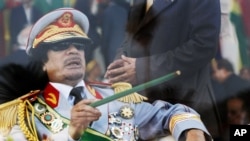 FILE - In this Tuesday, Sept. 1, 2009 file photo, Libyan leader Moammar Gadhafi gestures with a green cane as he takes his seat behind bulletproof glass for a military parade in Green Square, Tripoli, Libya.