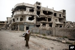 In this June 5, 2014 photo, a woman walks through a devastated part of Homs, Syria. Syrian government forces retook the control of Homs in May 2014, after a three year battle with rebels. (AP Photo/Dusan Vranic)