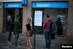 People line up at a Sabadell Bank ATM machine in Barcelona to withdraw money as part of a protest of the transfer of the bank's headquarters out of Barcelona, Spain, Oct. 20, 2017.