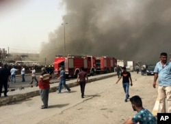 Smoke rises as Iraqi security forces and civilians gather at the scene of a deadly suicide car bomb attack in the Shiite-dominated neighborhood of New Baghdad, Iraq, Thursday, June 9, 2016.