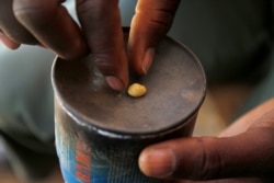 FILE - An artisanal gold miner picks up a gold nugget at an unlicensed mine in Gaoua, Burkina Faso, Feb. 13, 2018.