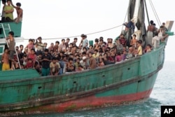FILE - Migrants including Myanmar's Rohingya Muslims sit on their boat as they wait to be rescued by Aceh fishermen on the sea off East Aceh, Indonesia, May 20, 2015.