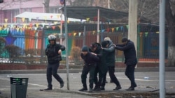 A police officer escorts a group of detained protesters in Almaty, Kazakhstan, Jan. 6, 2022.