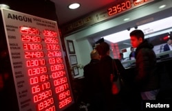 FILE - People check currency exchange rates at an exchange office in Istanbul, Dec. 16, 2014.