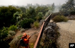 A firefighter from the California Conservation Crops Alder Camp works to put out wildfire hot spots, Dec. 16, 2017, in Montecito, Calif.