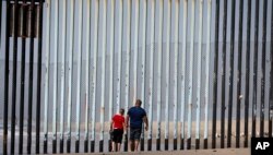 FILE - Two people walk towards metal bars marking the United States border where it meets the Pacific Ocean, in Tijuana, Mexico, March 2, 2016.