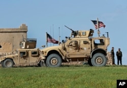 In this picture taken on March 29, 2018, a fighter, second from right, of U.S-backed Syrian Manbij Military Council stands next to U.S. humvee at a U.S. outpost north of Manbij town, Syria.