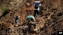 Residents carry food supplies along a landslide area near the site where dozens of victims are believed to have been buried in Itogon, Benguet province, northern Philippines, Sept. 19, 2018.