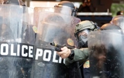 A policeman shoots rubber bullets at protesters throwing rocks and water bottles during a demonstration, May 30, 2020, in downtown in Miami, Florida.
