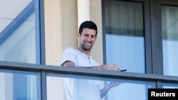 Bintang tenis Novak Djokovic berdiri di balkonnya di akomodasi tempat dia dikarantina sebelum Australia Terbuka di Melbourne, Adelaide Utara, Australia, 19 Januari 2021. (Foto: AAP/Morgan Sette via REUTERS)
