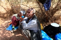 FILE - An Ethiopian refugee who fled fighting in Tigray province sits holding a radio in the shade of a straw shack at the Um Rakouba camp in Sudan, Nov. 18, 2020.