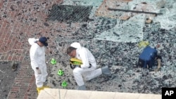 Two men in hazardous materials suits investigate the scene at the first bombing on Boylston Street near the finish line of the 2013 Boston Marathon, a day after two blasts killed three and injured more than 170 people, in Boston, April 16, 2013.