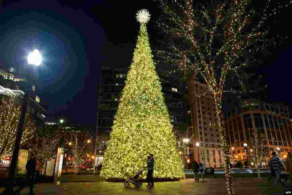 Una pareja y su bebé pasean frente a un árbol de Navidad en el centro de Washington, D.C., el 12 de diciembre de 2020. Las caminatas nocturnas para ver las decoraciones es algo a lo que muchos no renuncian pese al coronavirus. [AFP]