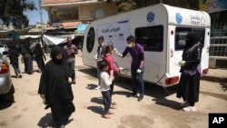 FILE - A member of a non-governmental aid organization measures temperature as a preventive measure for coronavirus in the town of Kafr Takharim, Idlib province, Syria.