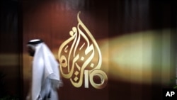 FILE - A Qatari employee of Al Jazeera Arabic language TV news channel passes by the logo of Al Jazeera in Doha, Qatar.