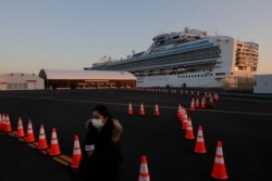 A CCTV reporter stands near the quarantined Diamond Princess cruise ship, Feb. 13, 2020, in Yokohama, near Tokyo. Life on board the luxury cruise ship, which has dozens of new virus cases, can include fear, excitement and soul-crushing boredom.