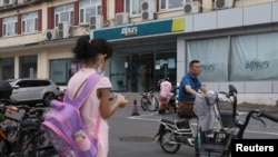 一个女孩站在北京街头一个新东方校外补习学校的附近。（2021年7月26日）