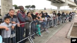 FILE - In this Sept. 26, 2019 file photo asylum seekers in Tijuana, Mexico, listen to names being called from a waiting list to claim asylum at a border crossing in San Diego. 