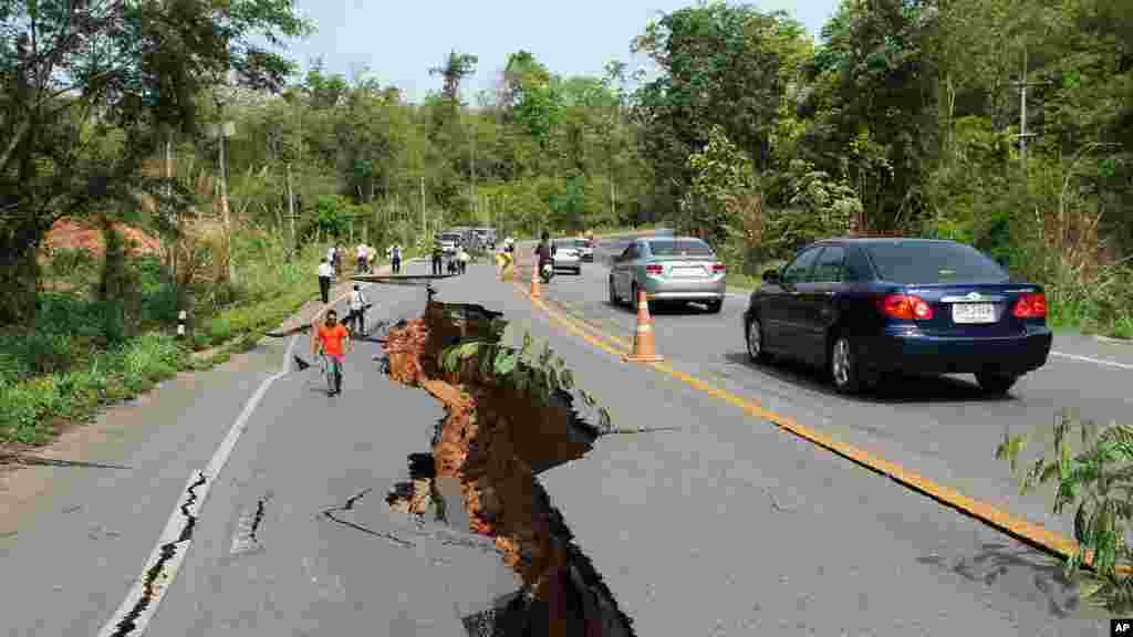 Motorists navigate their way around a cracked section of highway as people examine the damage after an earthquake, Chiang Rai, northern Thailand, May 6, 2014.