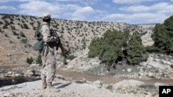 FILE - A Lebanon Hezbollah fighter carries his weapon as he stands in Khashaat, in the Qalamoun region after they advanced in the area, May 15, 2015. 