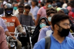 FILE - A woman wearing a face mask rides as a passenger on a motorbike amid a rush of people outside a market, amid the coronavirus pandemic, in Karachi, Pakistan, June 8, 2020.