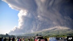 People watch as Mount Sinabung spews volcanic material during an eruption in Karo, North Sumatra, Indonesia, March 2, 2021. 