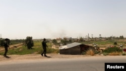 Shi'ite fighters from Saraya al-Salam, who are loyal to radical cleric Muqtada al-Sadr, stand guard on a road after a bomb attack against a state-run cooking gas factory in Taji at Baghdad's northern outskirts, Iraq, May 15, 2016. 