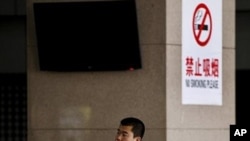 A Chinese man smokes in front of a pillar with a no smoking notice on display at a bus station in Beijing, March 24, 2011