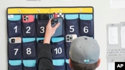 A ninth grader places his cellphone into a phone holder as he enters class Feb. 23, 2024, in Delta, Utah. Each classroom has a cellphone storage unit that looks like an over-the-door shoe bag with three dozen smartphone-sized slots.
