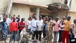 Onlookers gather around a car destroyed in a blast next to St. Theresa Catholic Church in Madalla, Nigeria, Sunday, Dec. 25, 2011. An explosion ripped through a Catholic church during Christmas Mass near Nigeria's capital Sunday, killing scores of people,