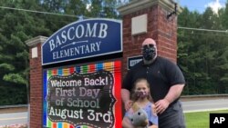 John Barrett and his daughter Autumn pose for photos outside Bascomb Elementary School in Woodstock, Ga., July 23, 2020. Barrett says he will educate his daughter virtually because of concerns about the spread COVID-19.