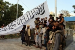 Taliban fighters pose for a photo while raising their flag at Ghazni provincial governor's house, in Ghazni, southeastern Afghanistan, Aug. 15, 2021.