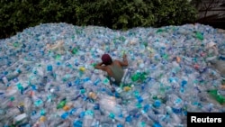 A worker uses a rope to move through a pile of empty plastic bottles at a recycling workshop in Mumbai June 5, 2014. 