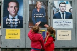 FILE - Children walk past election campaign posters for French centrist presidential candidate Emmanuel Macron and far-right candidate Marine Le Pen, in Osses, southwestern France, May 5, 2017.